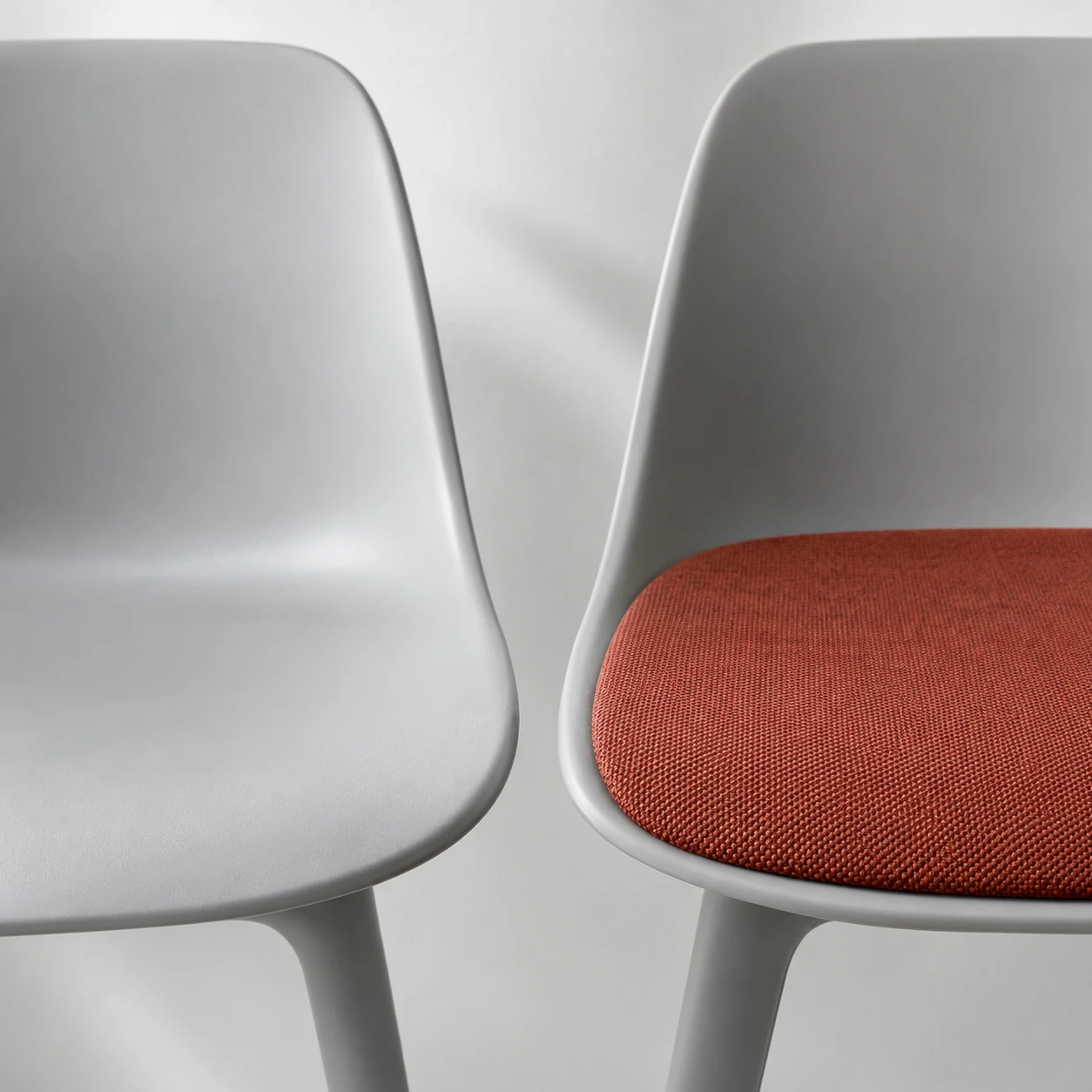 Bare grey chair shell beside a shell with a rust-coloured fabric seat pad